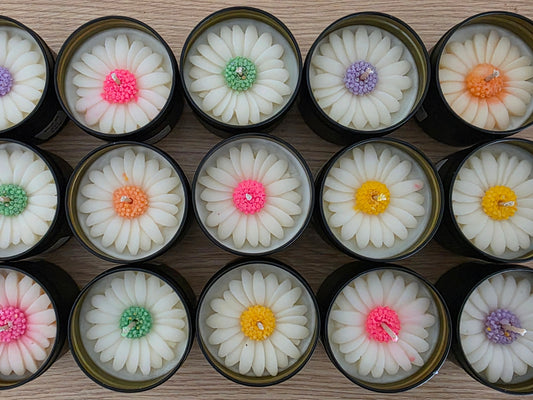 Assorted flower-shaped candles in small tins on a wooden surface