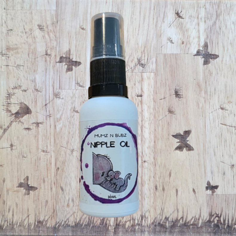 Spray bottle labeled 'Nipple Oil' on a wooden surface with dandelion designs.